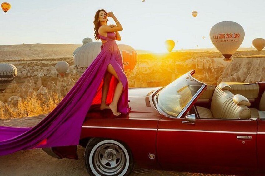 A woman in a purple dress sitting on a red convertible car with a long purple dress trailing behind her. 1