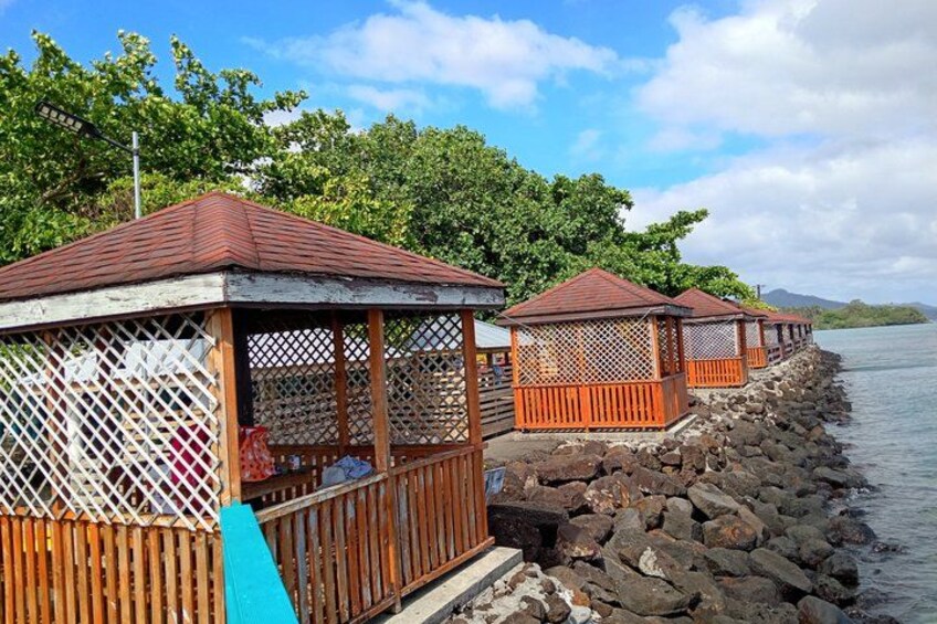 Gazebo in legno su una riva rocciosa, con acque calme e vegetazione lussureggiante sullo sfondo. 5