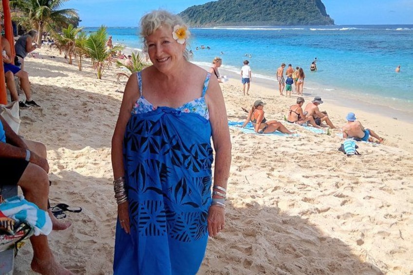 Una spiaggia con persone che prendono il sole, una donna con un vestito blu e un mare cristallino. 2