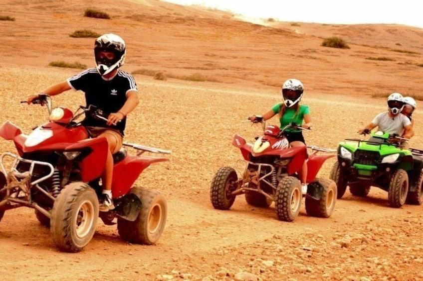 Three people riding ATVs on a dirt road in a desert landscape. 2