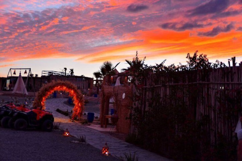 A sunset at a beach with a wooden archway, tiki torches, and a fenced area. 5