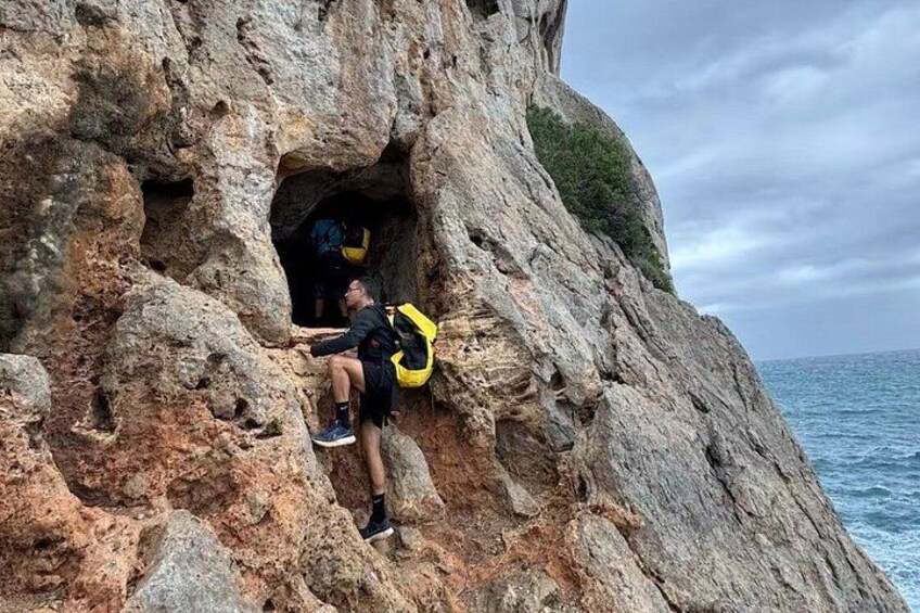 A person climbing a rocky cliff with a cave entrance. 1