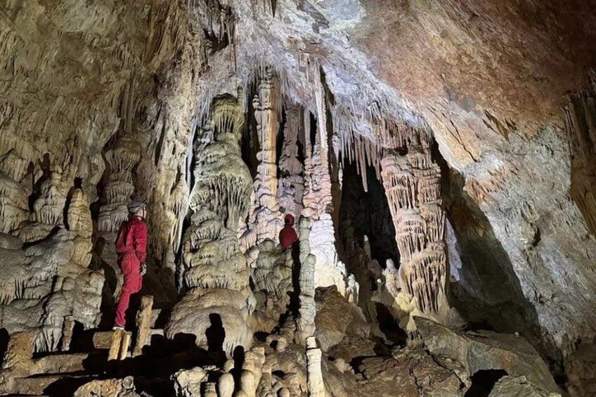 A cave with stalactites and stalagmites, people exploring, and a person in a red outfit. 3