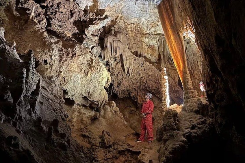 A person in red standing in a cave with stalactites and stalagmites. 5