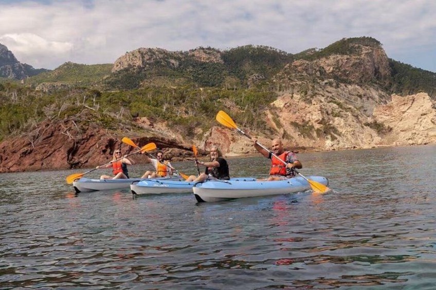 Three kayaks on calm water with a rocky coastline and hills in the background. 1