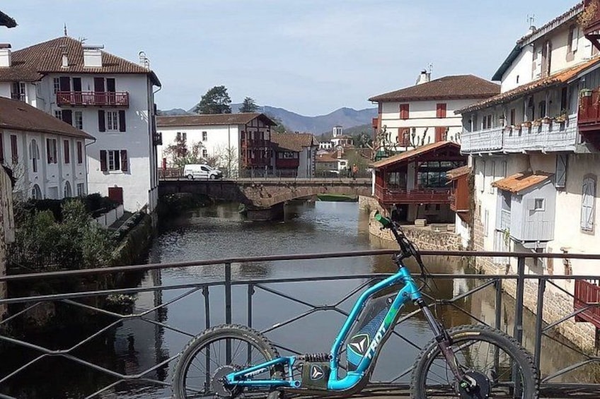 A bicycle parked by a canal with buildings and a bridge in the background. 1