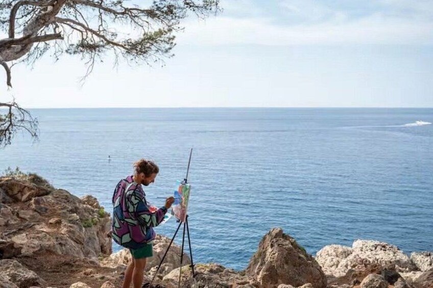 A person painting on a rocky seaside with the ocean in the background. 1