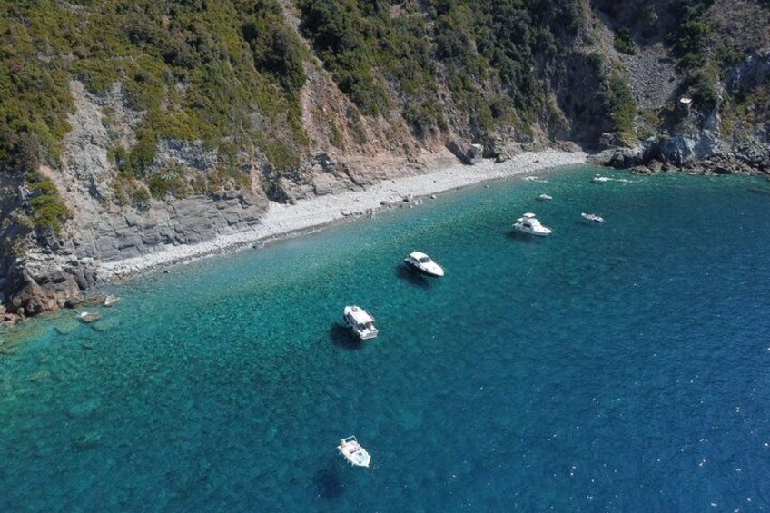 A coastal area with boats anchored in clear blue waters, rocky cliffs, and a sandy beach. 4