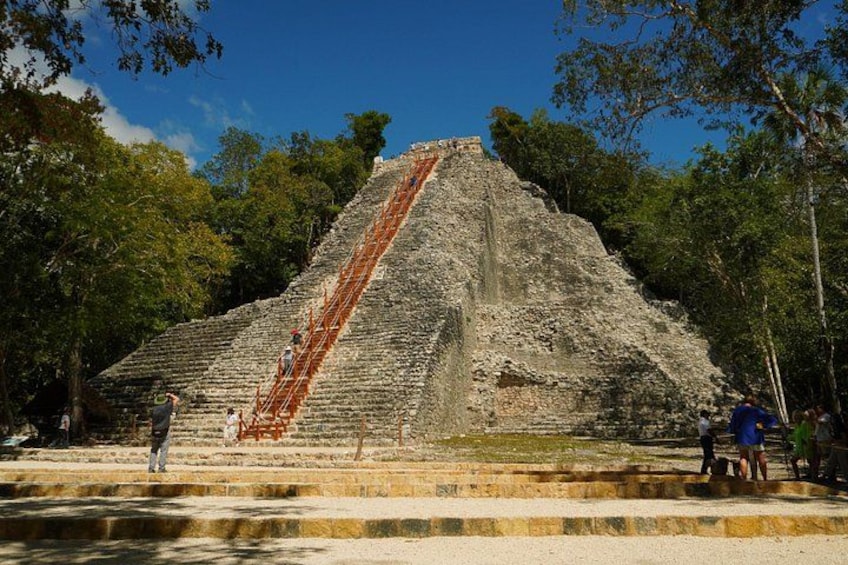 A large pyramid with a long staircase leading up to the top, surrounded by trees. 1