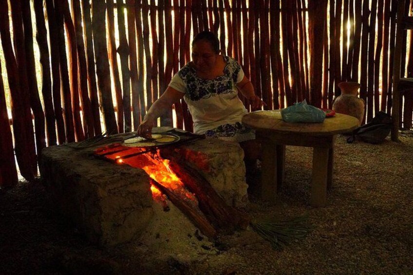 A person cooking over an open fire, with a table and a woven bamboo backdrop. 5