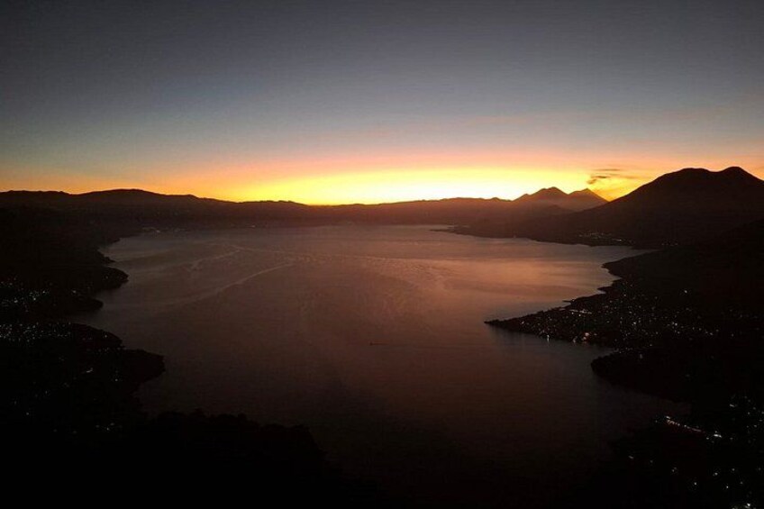 A sunset over a calm body of water with surrounding hills. 1
