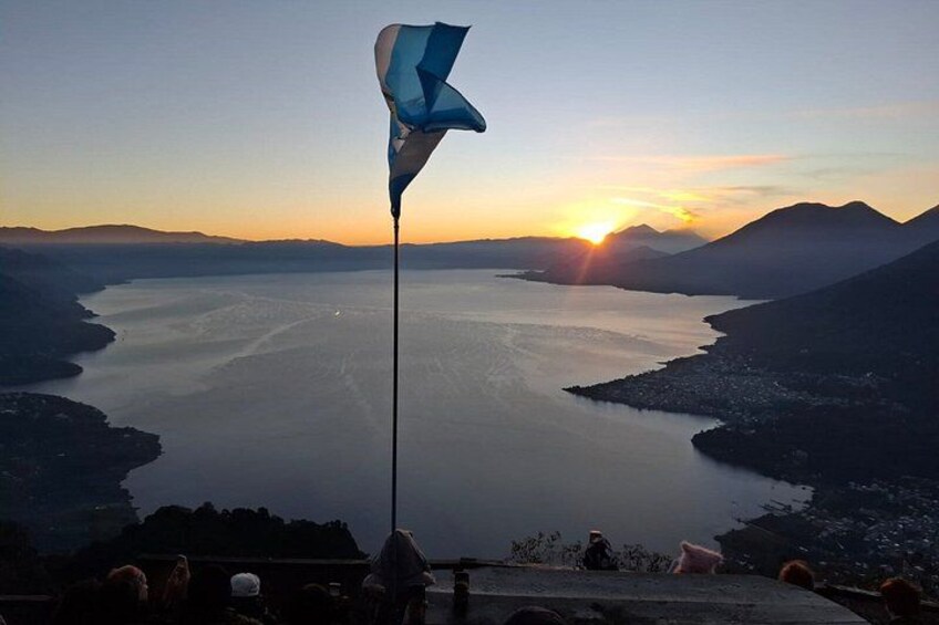 A flag on a pole, a body of water, and mountains in the background. 4
