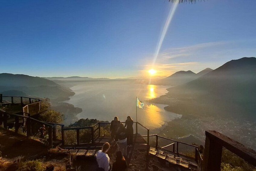 A sunset over a river with mountains in the background and a viewing platform with people. 3