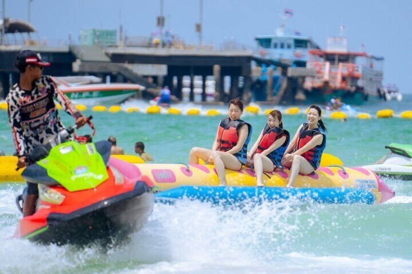 A jet ski with three people on an inflatable raft, water sports activity, pier, boats, and dock in the background. 1