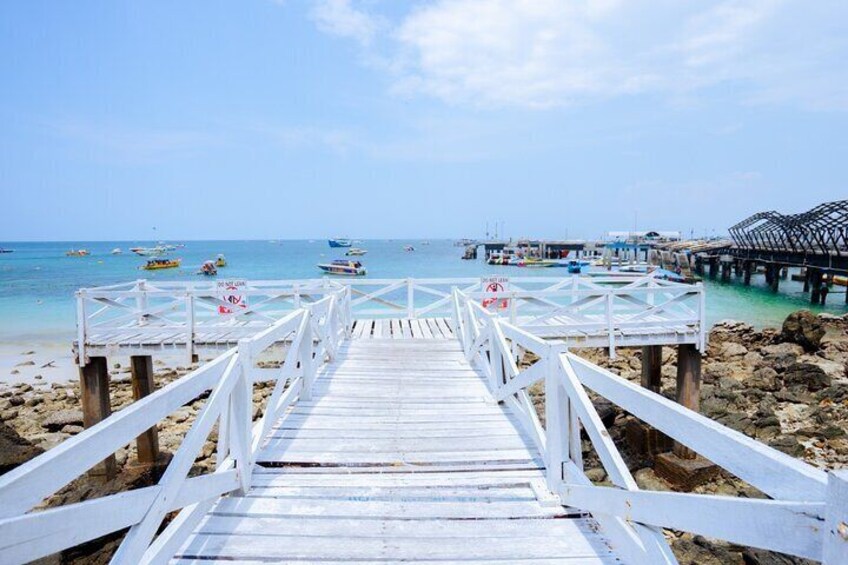 A wooden pier leading to a beach with boats and a pier structure in the background. 3