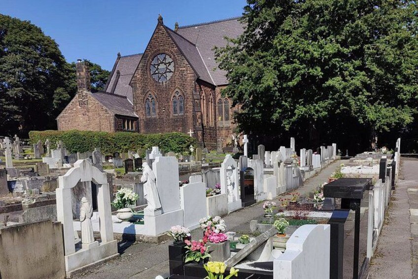 A cemetery with headstones, a church, and a large tree. 5