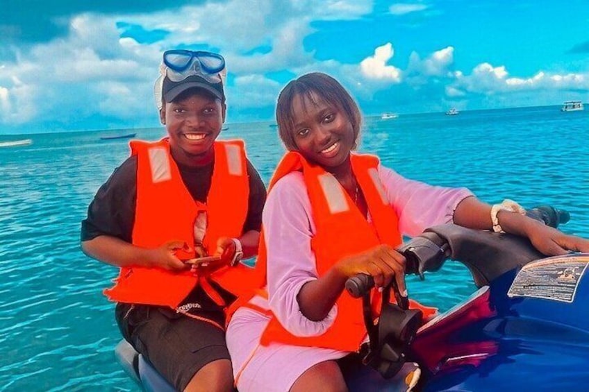 Two people in orange life vests on a boat in the ocean. 3