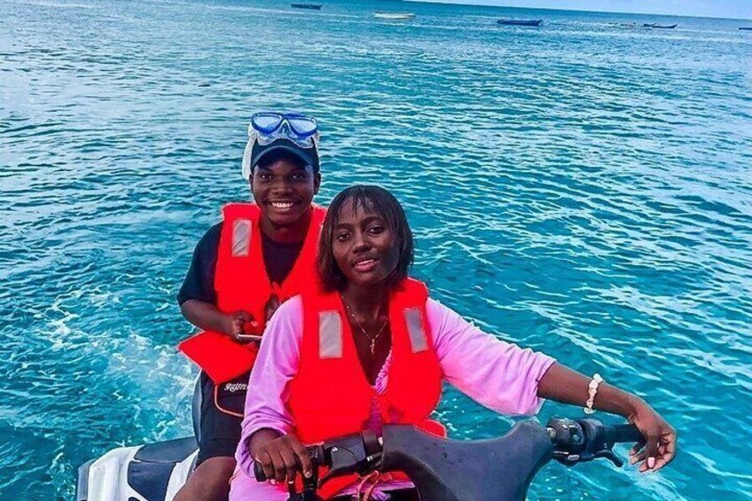 Two people on a jet ski in turquoise water with boats in the background. 2
