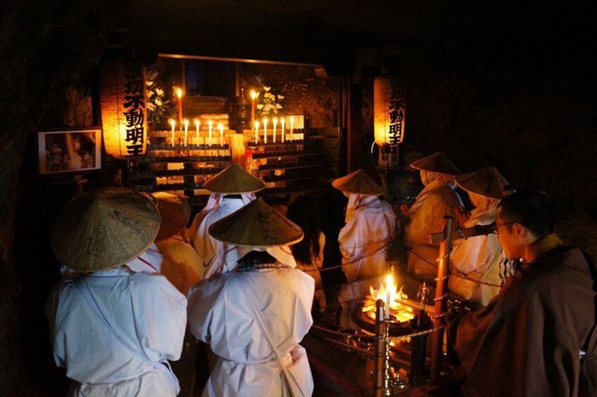 People in traditional attire with conical hats, gathered around a lit altar in a dimly lit room. 3