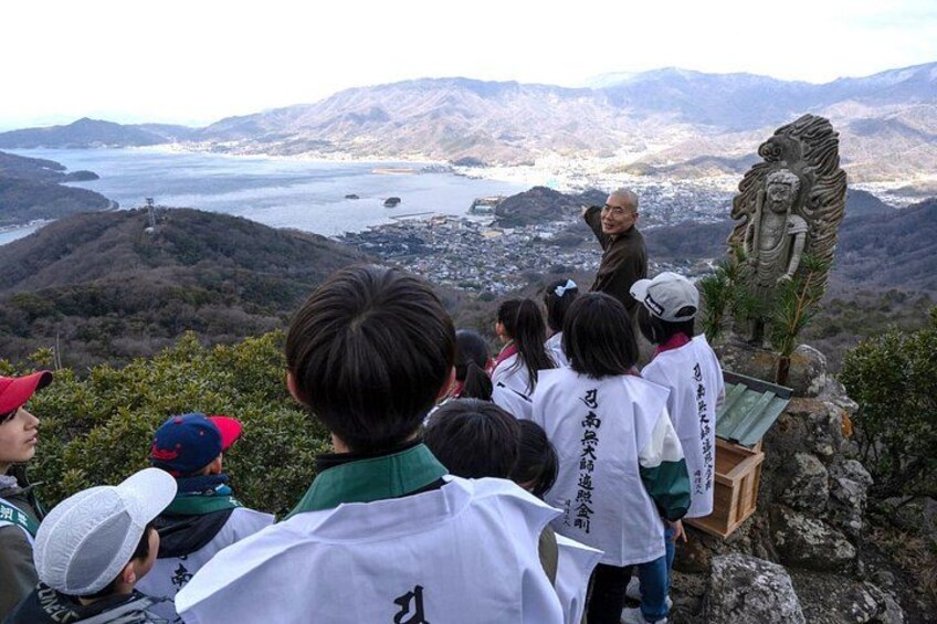 A group of people at a scenic overlook with a statue and a view of a valley. 4