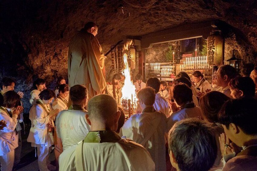 A group of people gathered around a fire in a cave-like setting, with a person standing on a platform. 1