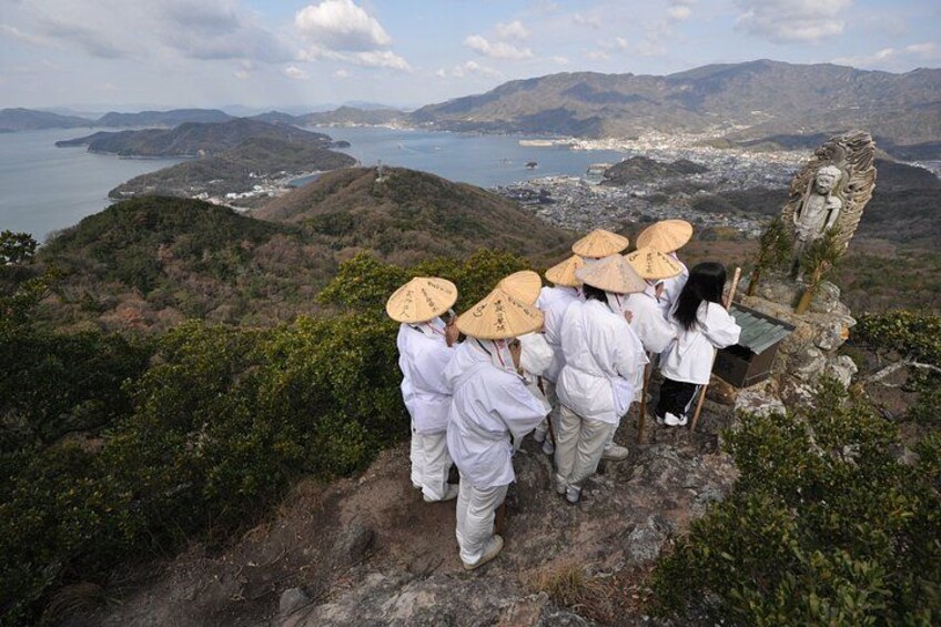 A group of people wearing white and straw hats, standing on a rocky path with a view of a coastal landscape. 2