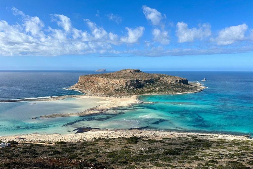 A coastal landscape with a prominent rocky island, clear turquoise waters, and a sandy beach. 1