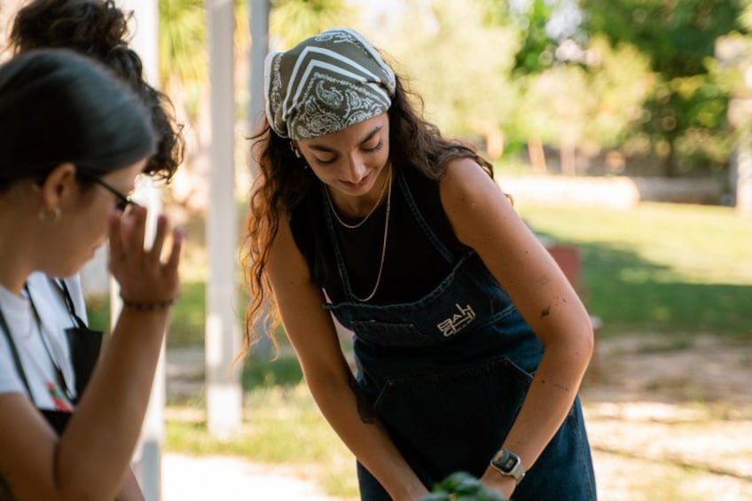 A person wearing a bandana and a sleeveless top, standing outdoors with greenery in the background. 3