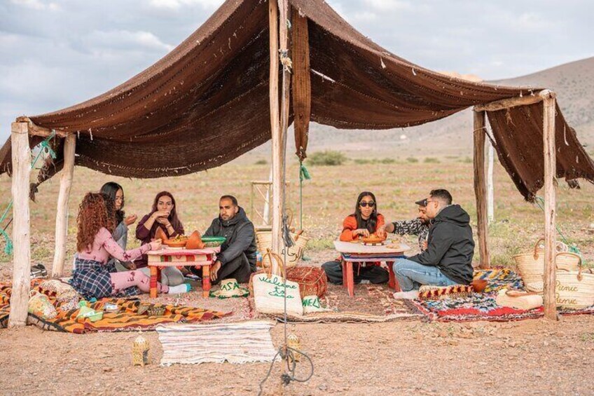 A group of people sitting around a table under a tent in a desert setting. 2