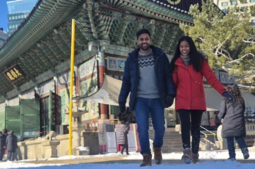 Una pareja caminando de la mano en un área nevada con arquitectura tradicional. 3