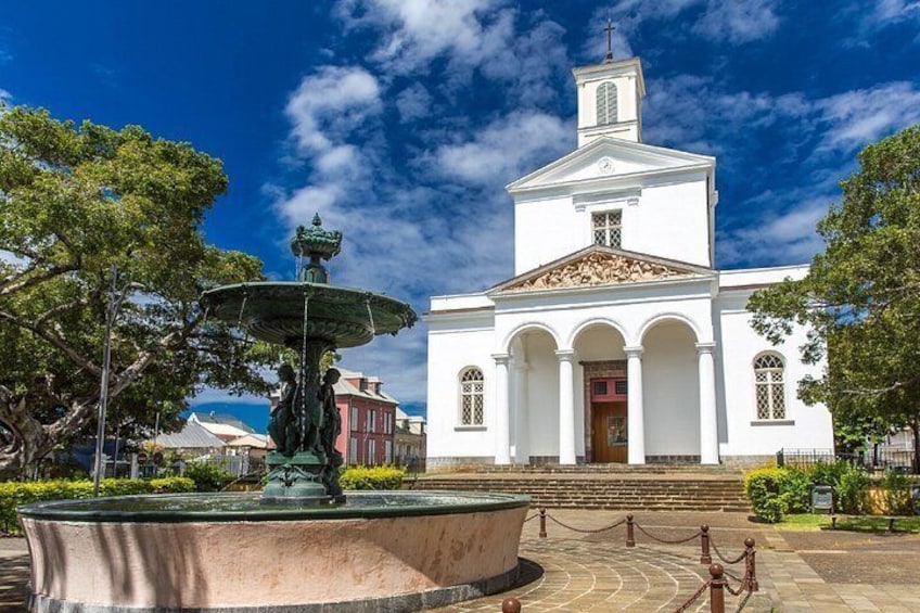 A white church with a bell tower, a fountain, and trees in the foreground. 4