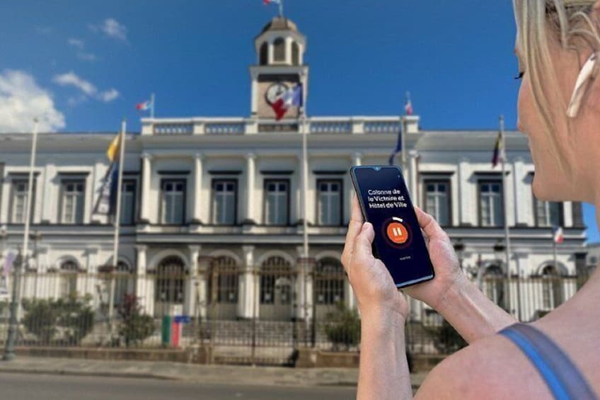 A person holding a smartphone with a map application, standing in front of a historic building with a clock tower. 5