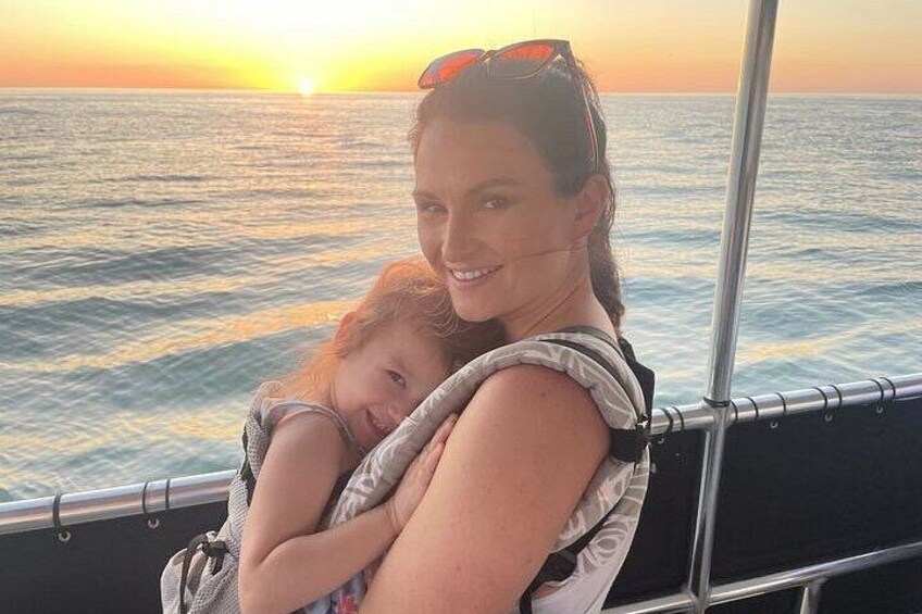 A person holding a child on a boat with a sunset in the background. 3