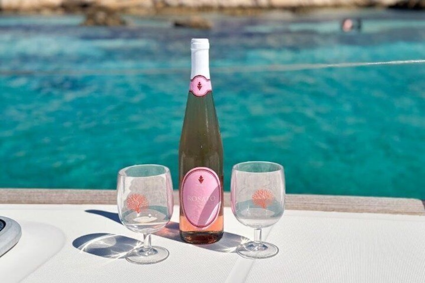 A bottle of rosé wine with a pink label, two wine glasses, and a table by a poolside. 3