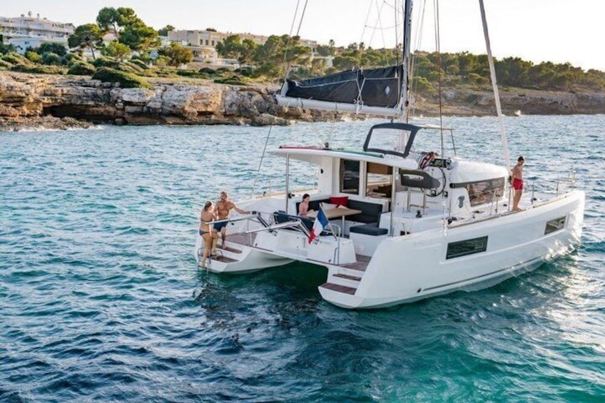 A white sailboat with people on deck, calm water, and a rocky coastline with buildings in the background. 5