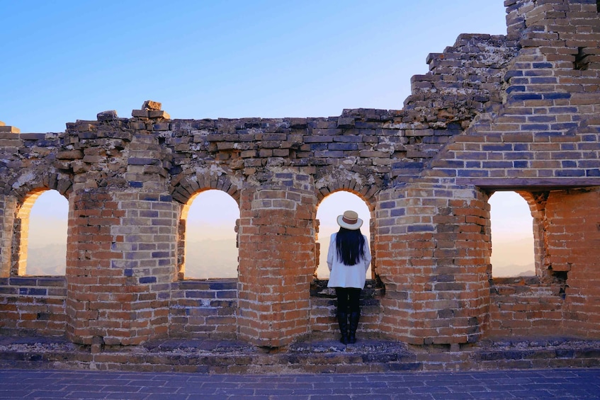 A person standing in front of a brick wall with arched openings. 4