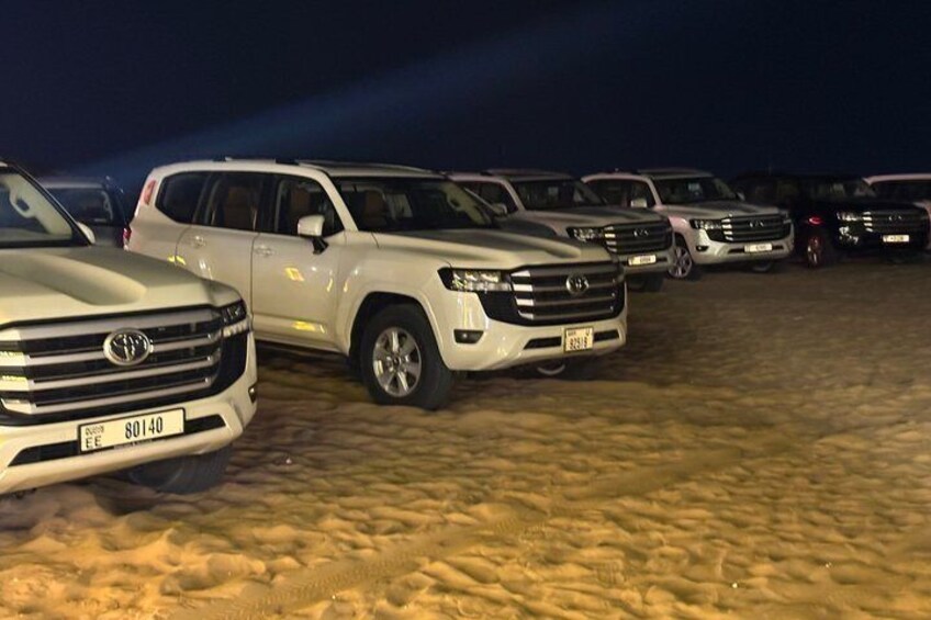 A row of parked SUVs on a sandy surface at night. 2