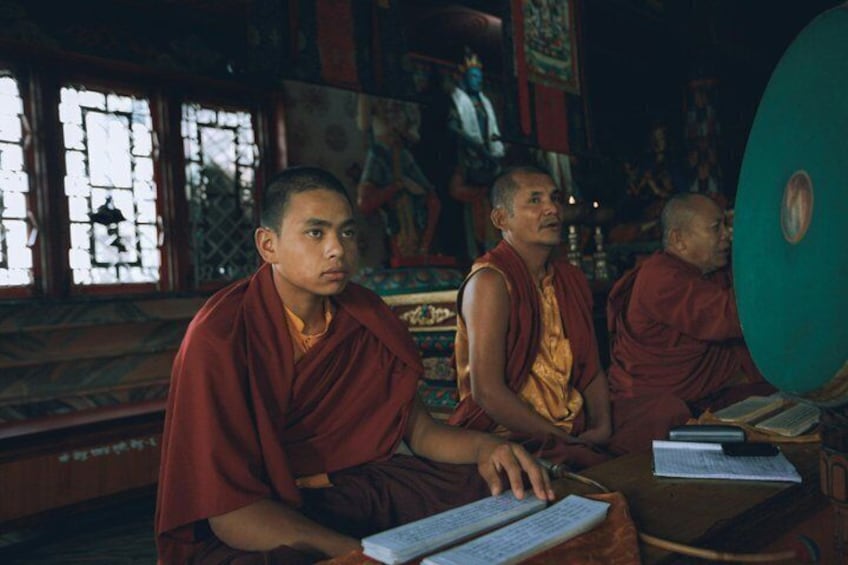 Monjes con túnicas tradicionales sentados en un templo con ruecas de oración y pinturas religiosas. 5