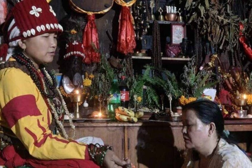 A person in traditional attire sitting at a table with various items, including a lit candle, fruits, and decorative objects. 4