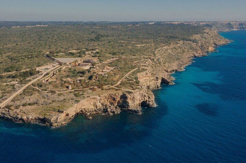 An aerial view of a coastal area with rocky terrain, a clear blue sea, and scattered buildings. 4