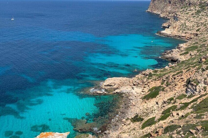 A coastal landscape with clear turquoise waters, rocky terrain, and sparse vegetation. 5