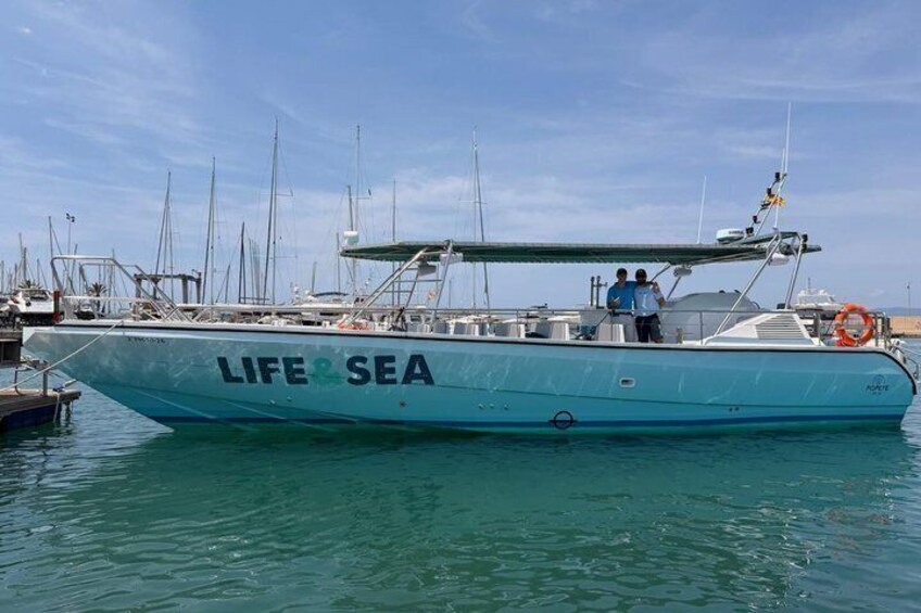 A boat named 'LIFE & SEA' docked at a marina with other boats in the background. 2