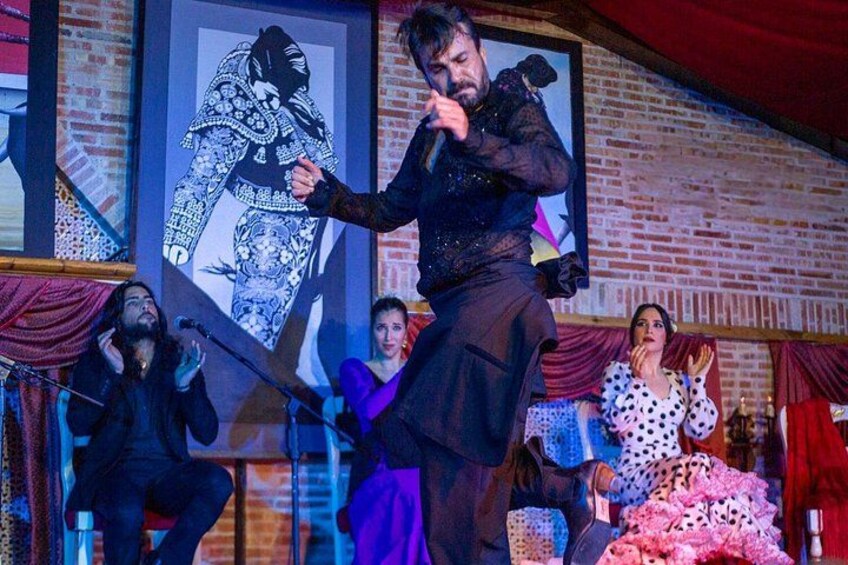 A person performing on stage with a microphone, surrounded by a brick wall and framed artwork. 3