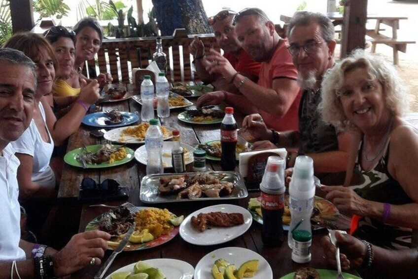 A group of people dining at an outdoor table with various dishes and drinks. 2
