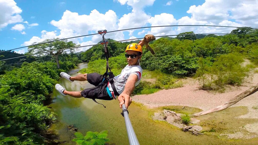 A person zip-lining over a river with lush greenery and a clear sky. 1