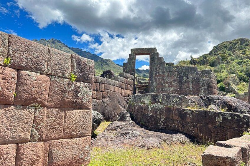 Ancient stone ruins with a stone archway, surrounded by mountains and greenery. 1