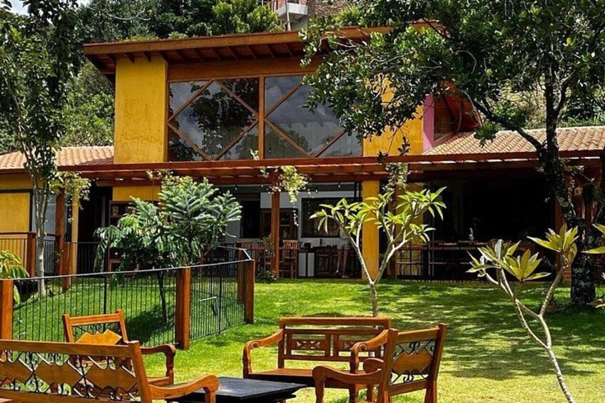 A yellow building with a tiled roof, surrounded by a well-maintained lawn and wooden furniture. 2
