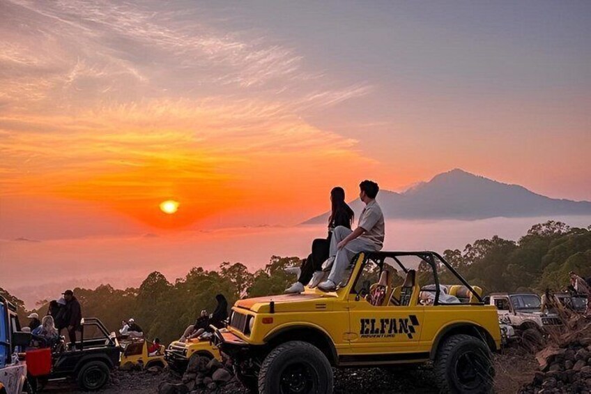 Un coucher de soleil avec un couple à bord d’un véhicule tout-terrain jaune, entouré d’autres véhicules et de personnes. 1