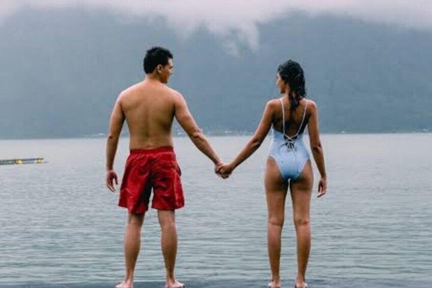 Two people holding hands on a lakeshore with a boat in the background. 3