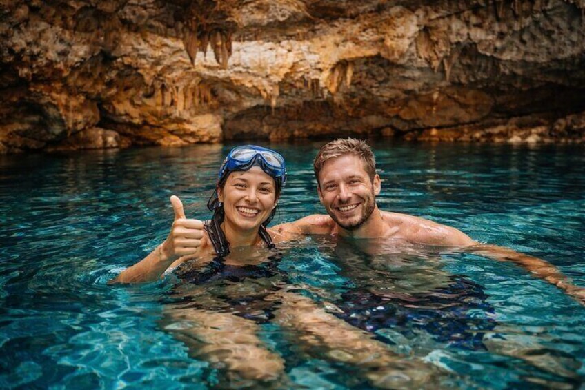 Two people in a clear blue pool with a rocky cave background. 3